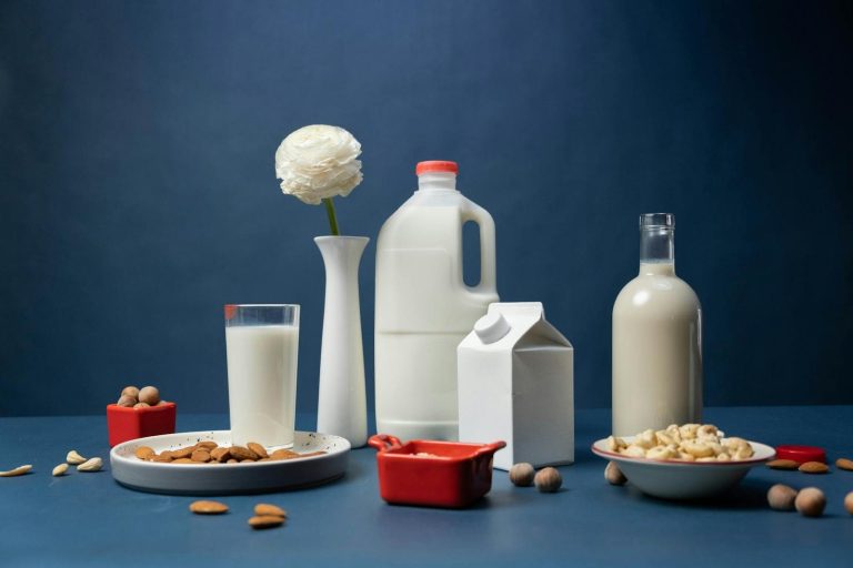 Still life of assorted vegan nut milks with nuts and decorative flower in studio.