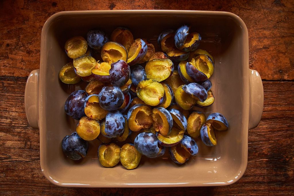 Top view of juicy sliced plums in a rustic baking dish on a wooden table, perfect for baking or cooking.