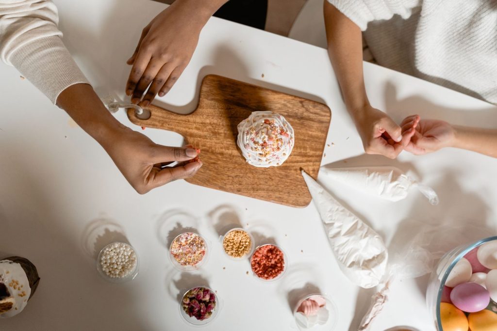 Top view of hands decorating cupcakes with icing and sprinkles.