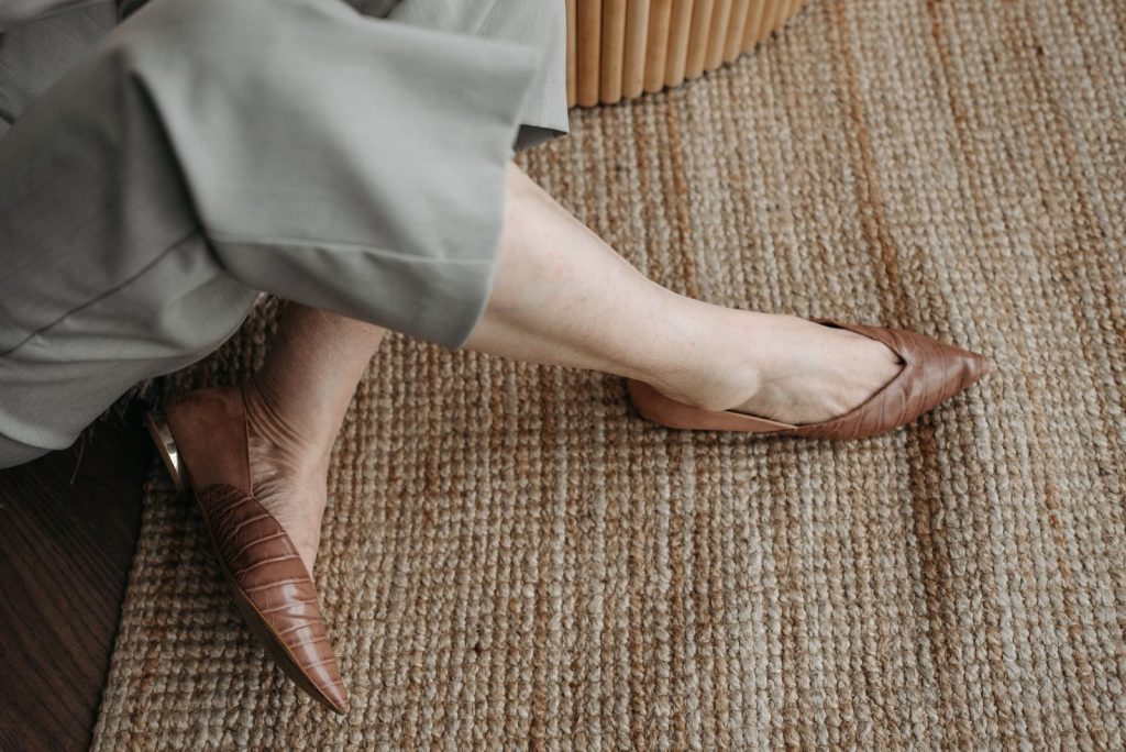 Close-up image of brown leather flats and light trousers on a woven carpet.