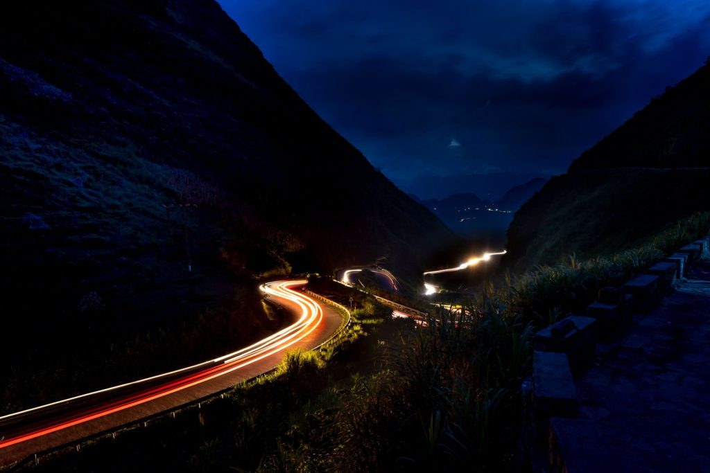 Illuminated mountain road with curving light trails under a dark night sky.