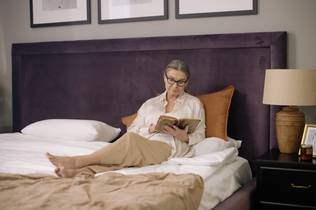 A senior woman enjoys reading a book in a cozy and elegant bedroom setting.