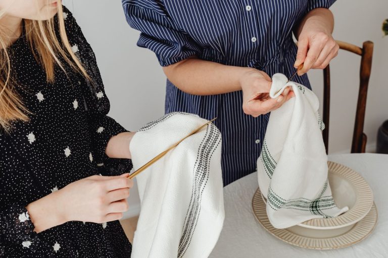 Two women carefully cleaning cutlery and setting a table with white linens.