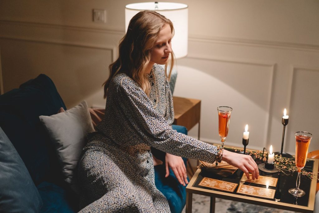 Adult woman with long hair playing cards on a table, with drinks and candles.
