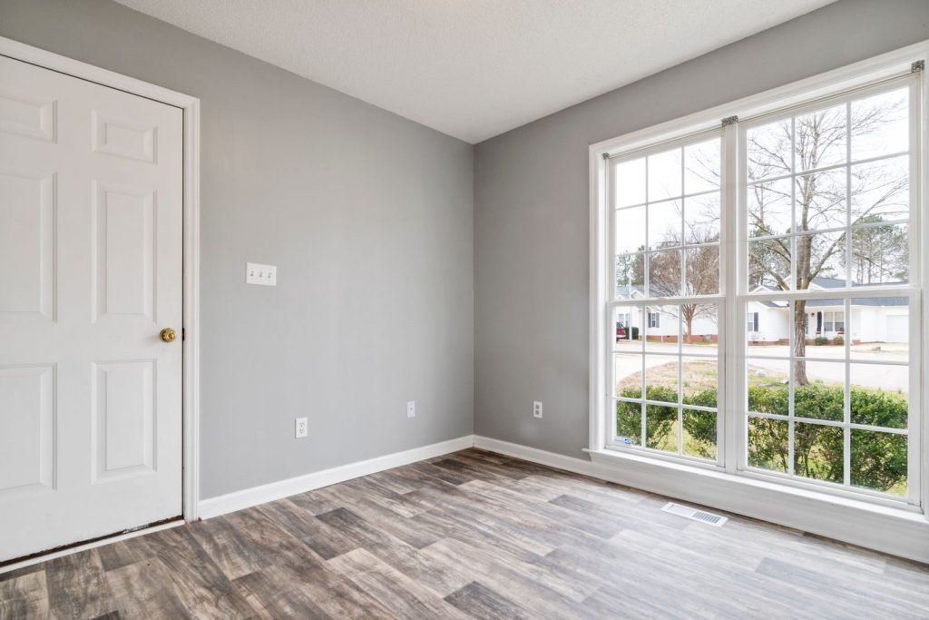 Bright and spacious empty room with wooden flooring and large window, perfect for residential property listings.
