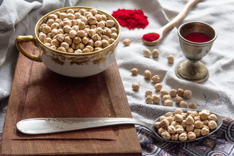 Chickpeas in a cup on a wooden board with spices, showcasing a rustic food preparation setup.