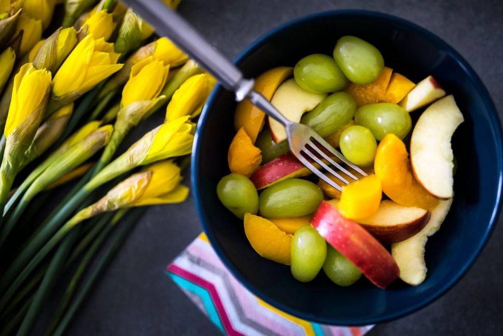 Vibrant fruit salad in a blue bowl with fresh daffodils nearby, showcasing a spring vibe.