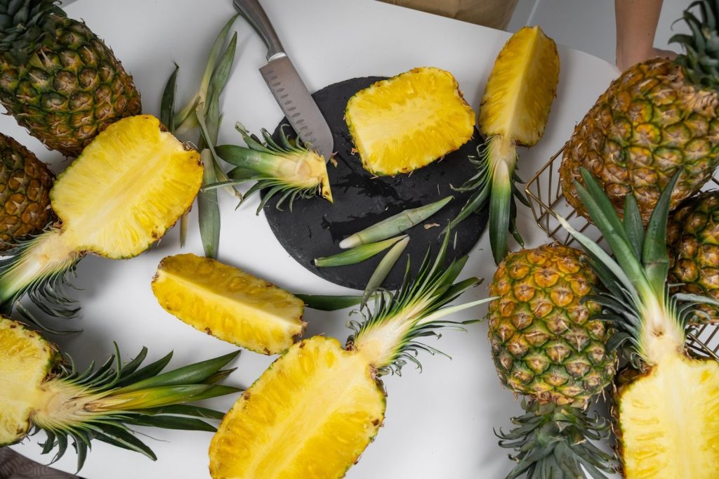 From above of table with cut fresh pineapples with juicy flesh and leaves on cutting board in house