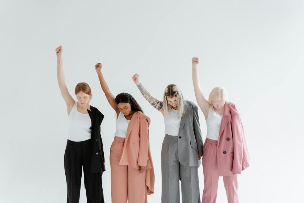 Four diverse women in business attire raise fists in unity on a white background.
