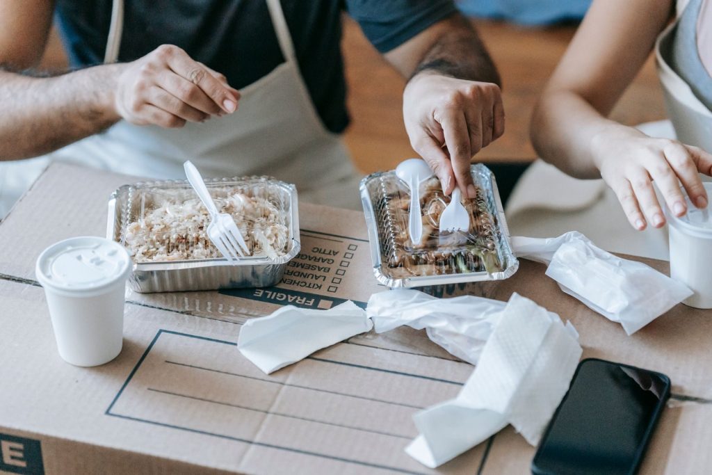Couple savoring takeout meals on moving day, sitting over packing boxes.