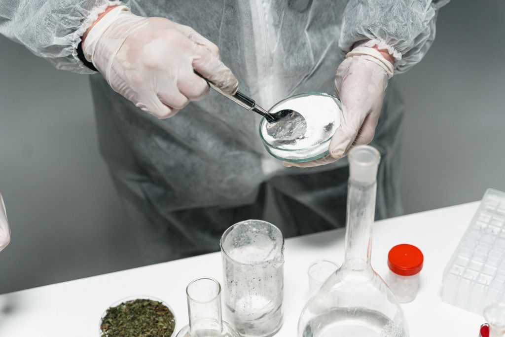 Scientist in protective gear handling powder sample in a sterile lab environment.