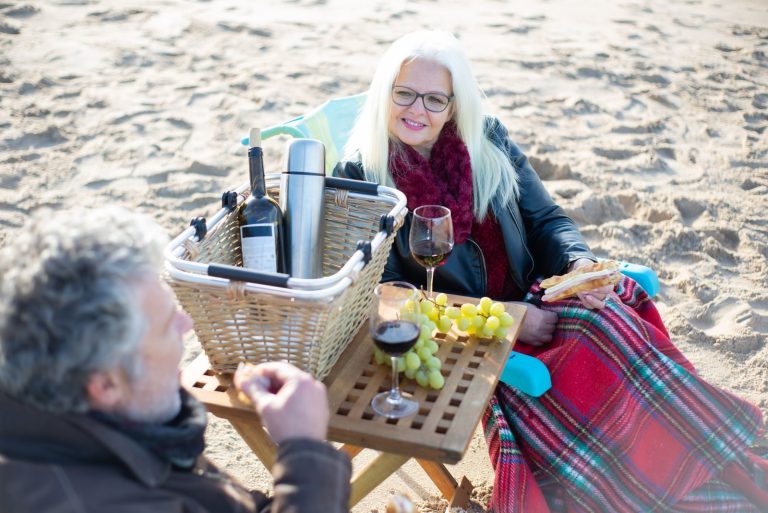 Warm beach afternoon with elderly couple having a picnic on sandy shores in Portugal, featuring wine and grapes.