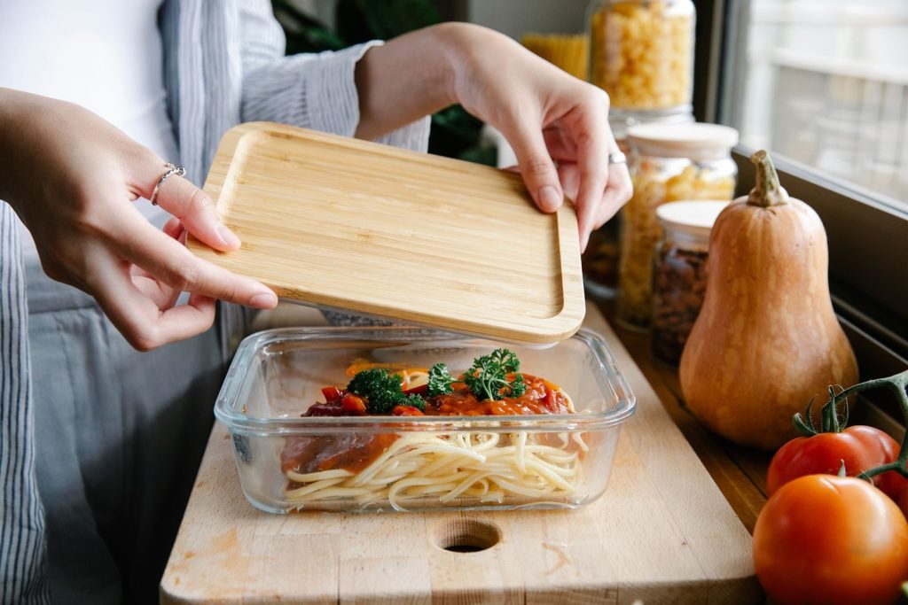 From above of crop faceless female covering glass bowl with freshly prepared pasta with tomato sauce while preparing delicious dinner in kitchen