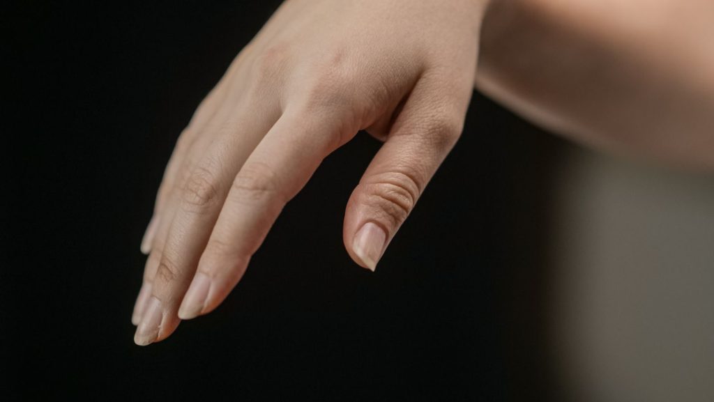 Detailed image of a hand with natural nails, delicately posed against a dark backdrop.
