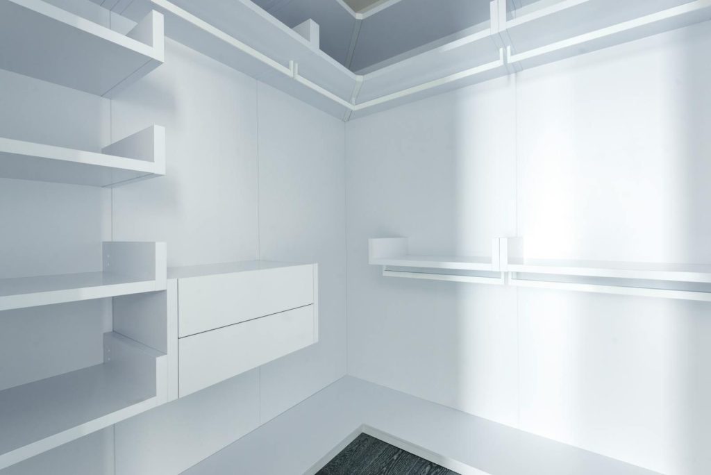 Modern minimalist walk-in closet with white shelves and bright lighting.