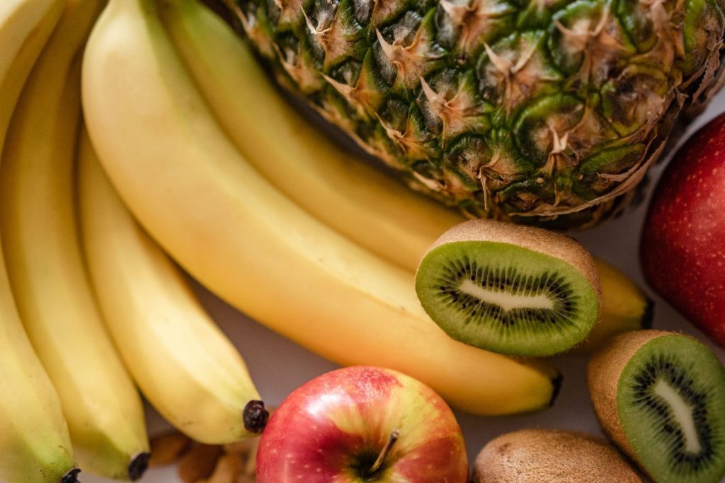 From above of bunch of ripe bananas apples near halved kiwi and pineapple