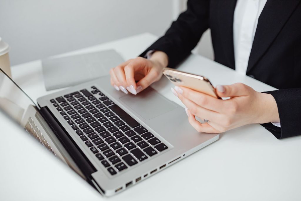 Professional woman in business attire using a laptop and smartphone at a desk.