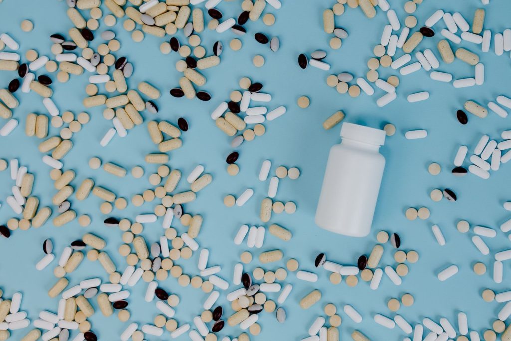 Top view of various pills scattered around a white bottle on a blue surface.