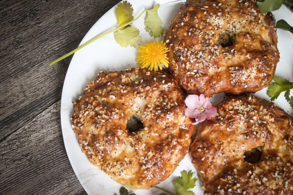 Delicious bagels topped with sesame seeds and garnished with flowers on a white plate.