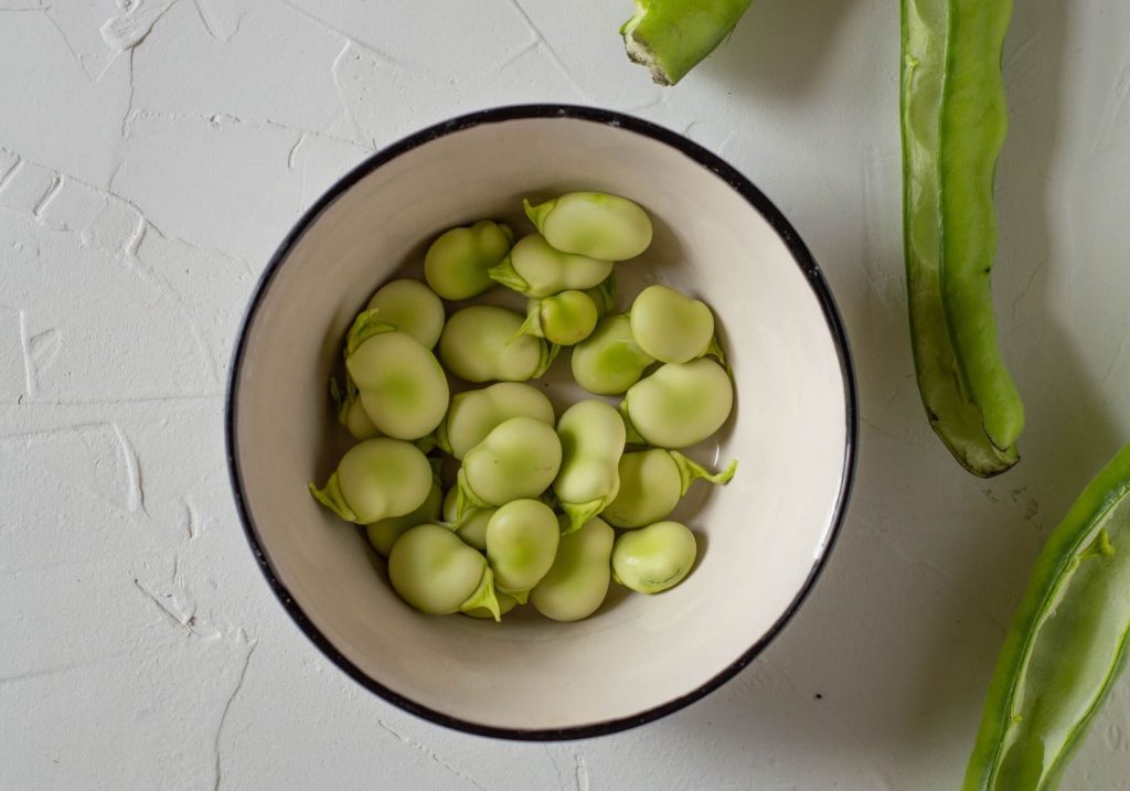Overhead shot of fresh broad beans in a ceramic bowl, showing healthy green legumes.