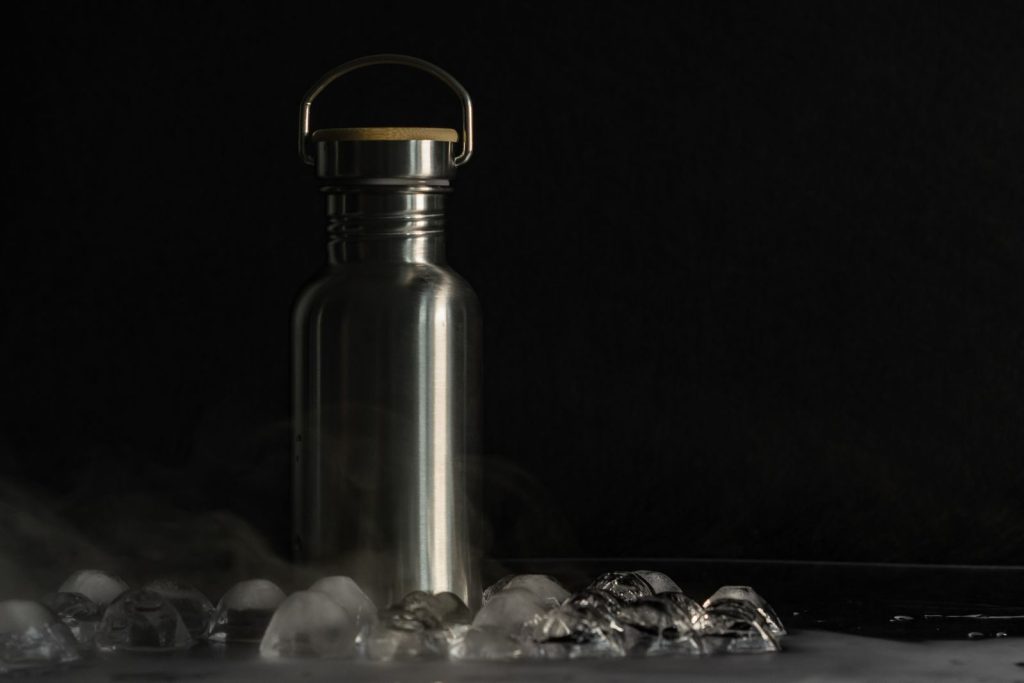 A stainless steel flask surrounded by ice cubes on a dark surface, offering a minimalist and sleek aesthetic.