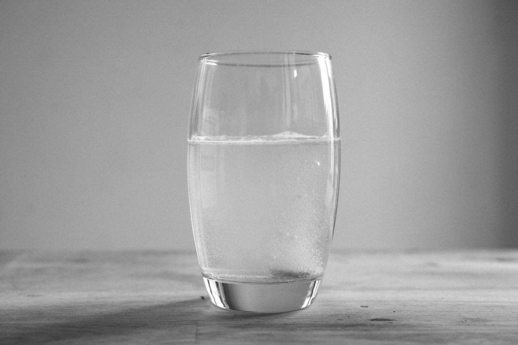 Minimalistic black and white photo of a glass of water on a wooden surface, captured indoors.
