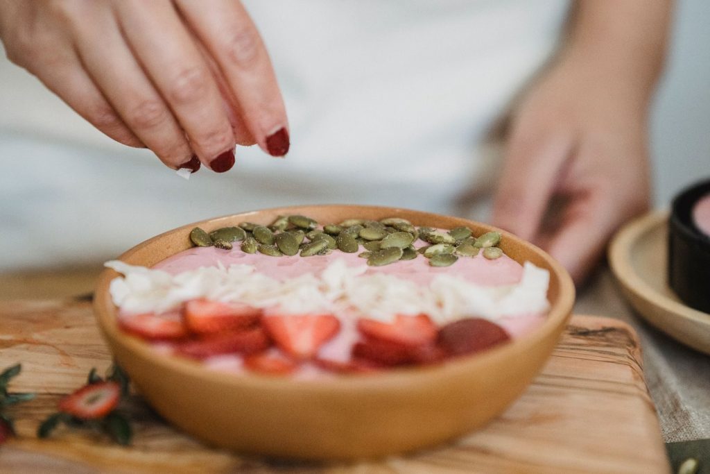 Hand garnishing a smoothie bowl with seeds, featuring strawberries and coconut flakes.