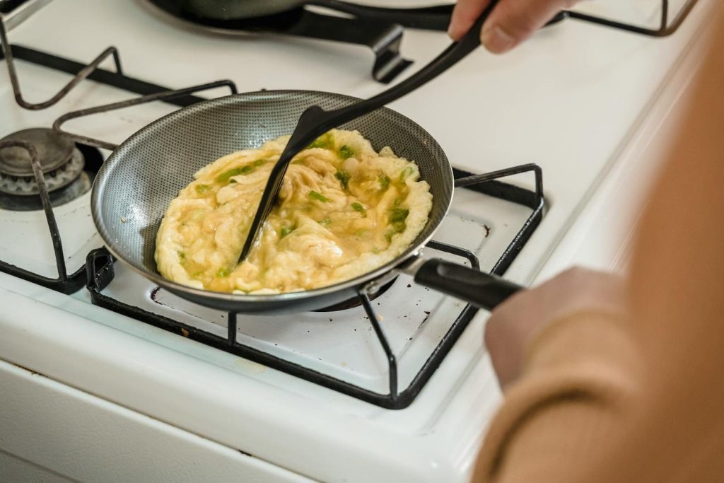 Close-up of scrambled eggs being cooked on a gas stove using a spatula.