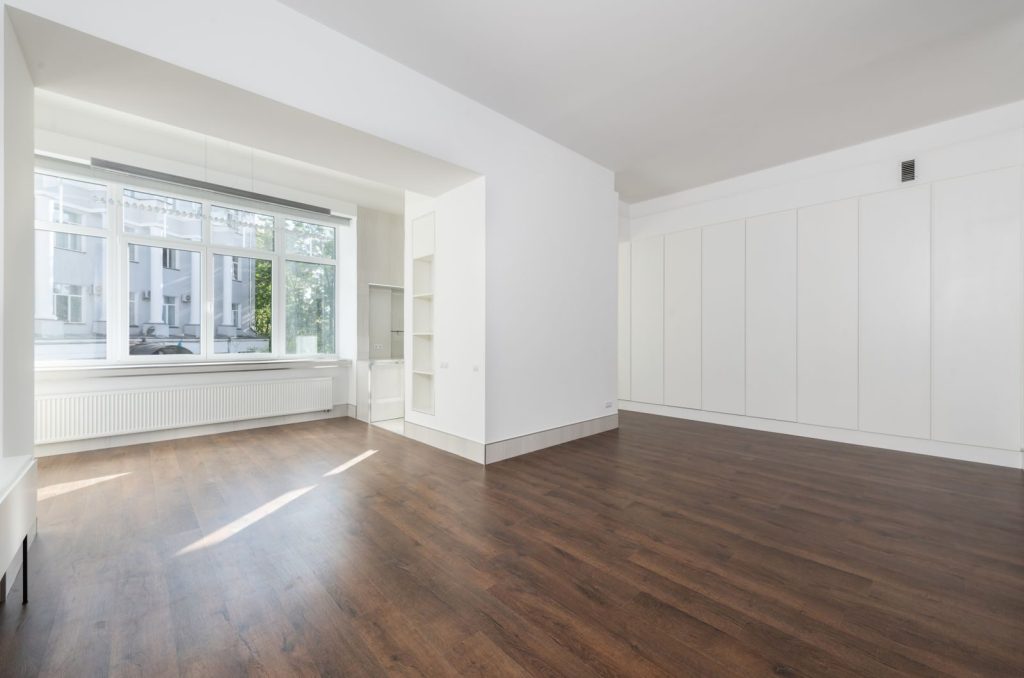 Bright empty room featuring large windows and wooden flooring.