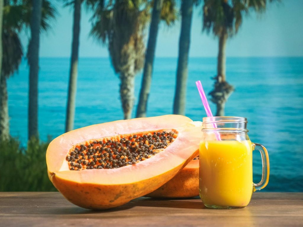 Refreshing papaya next to a tropical juice with seaside backdrop, exuding summer vibes.