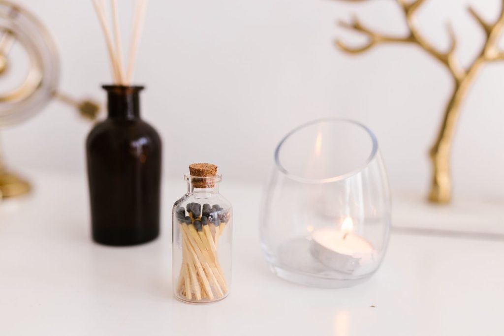 Aesthetic arrangement of matches, glass candle holder, and decor on a white surface.