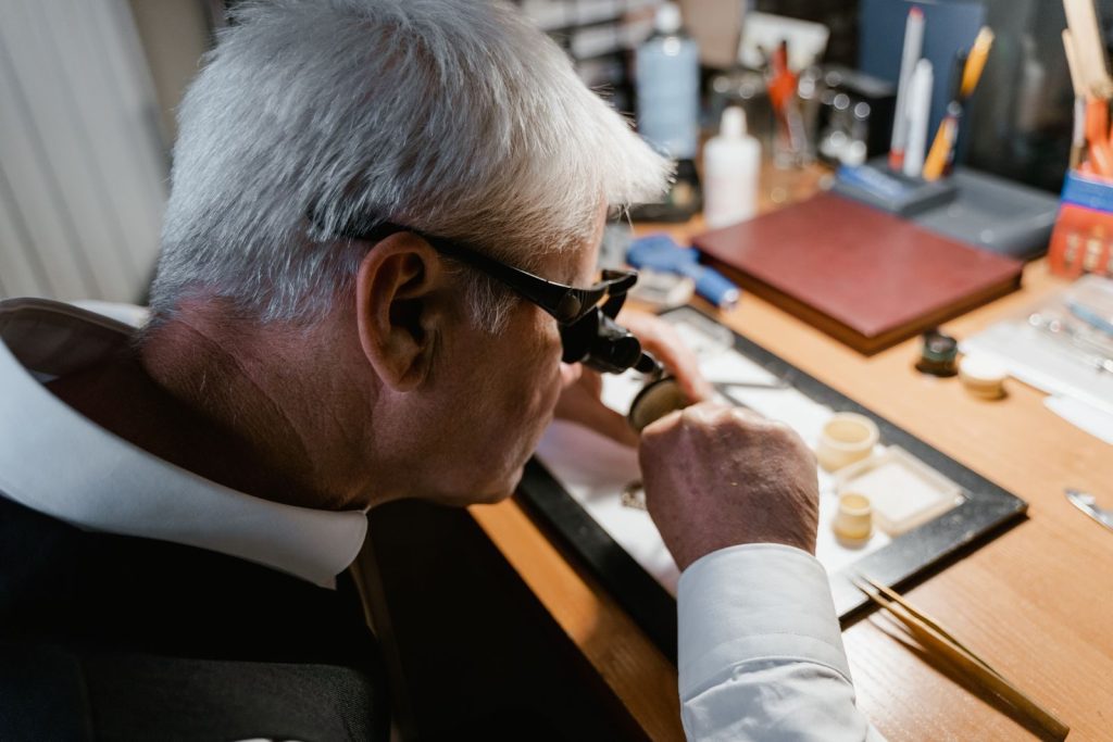 Senior watchmaker carefully examining a timepiece with a loupe in workshop.
