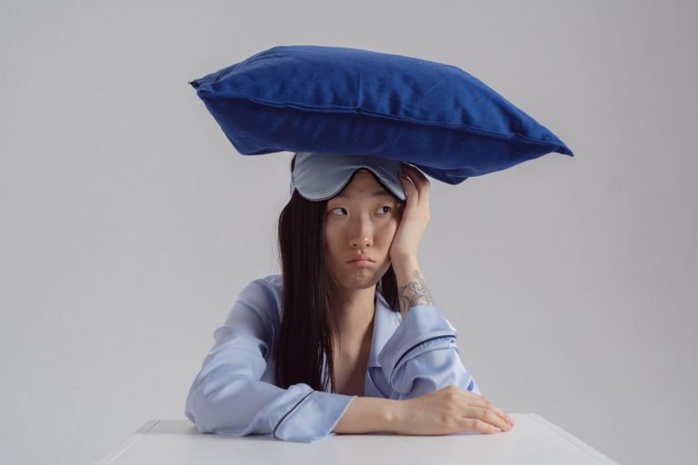 Tattooed woman with pillow and sleep mask showing insomnia concept.