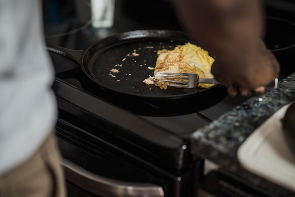 Man cooking omelet in a pan on a stove, showcasing a home-cooked meal setting.