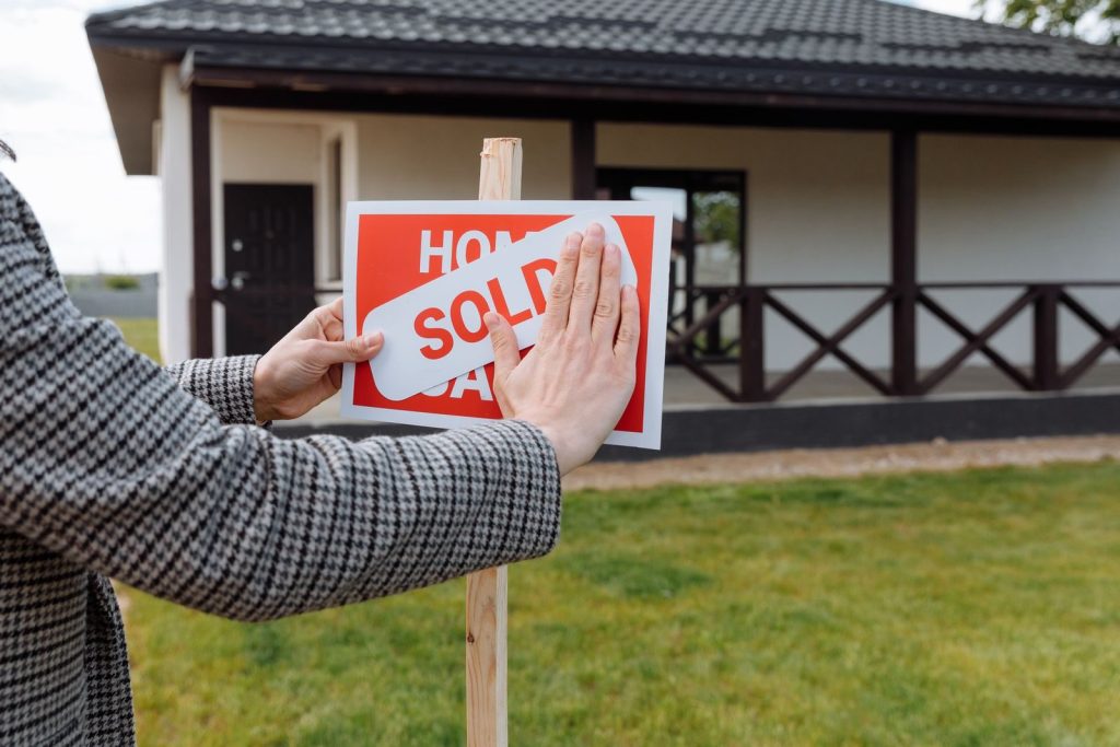 Close-up of hands placing 'sold' sticker on sign in front of a new house.