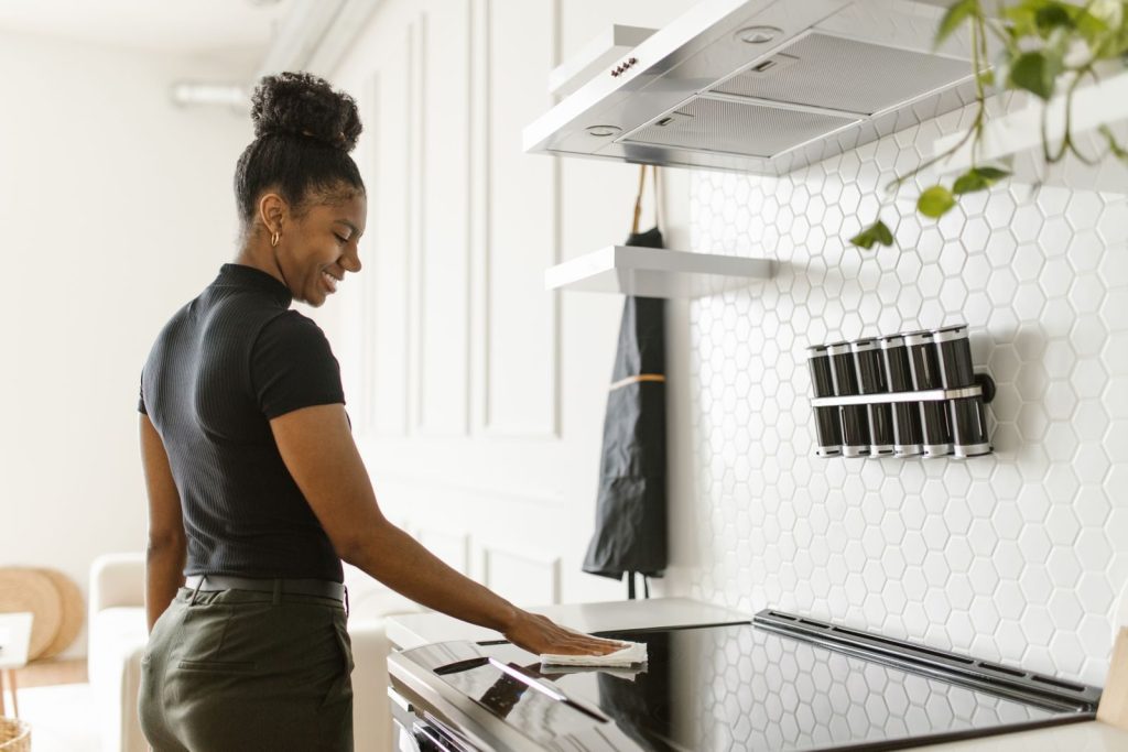 A woman cheerfully cleans her kitchen, focusing on the electric stove in a bright, modern space.