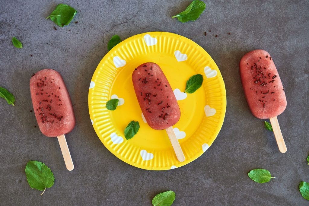 Top view of strawberry popsicles on a vibrant yellow plate with scattered mint leaves, perfect for dessert lovers.
