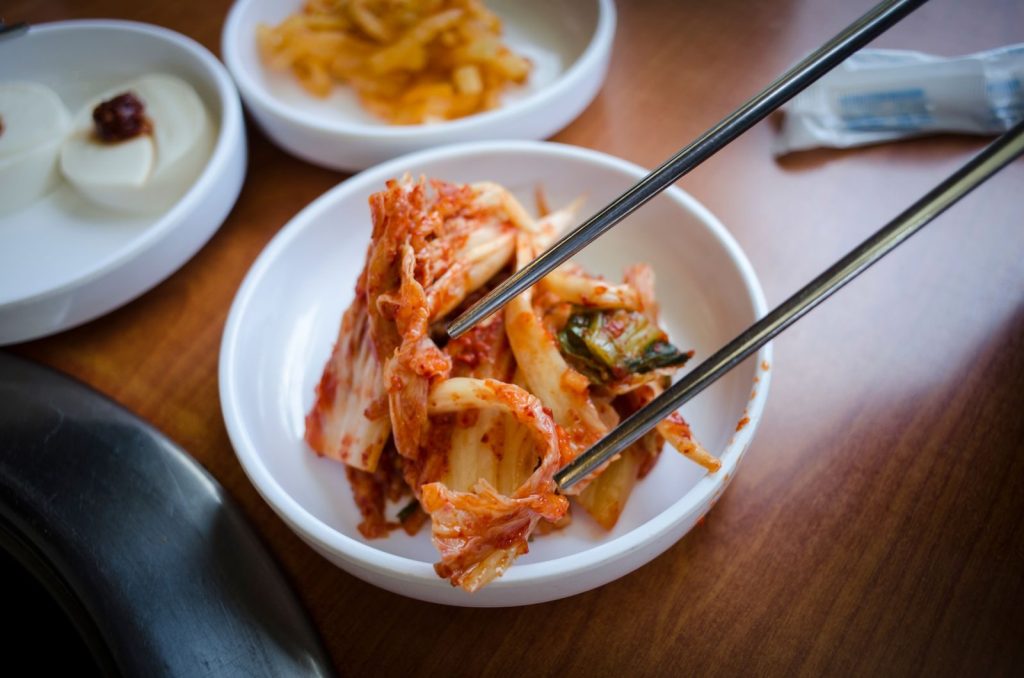 Close-up of traditional Korean kimchi in a ceramic bowl with chopsticks on a wooden surface.