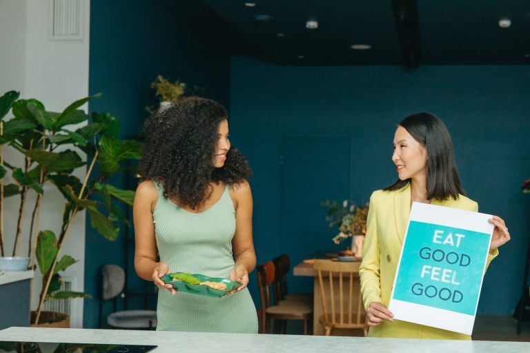 Two women discussing healthy eating with a sign and vegetables.
