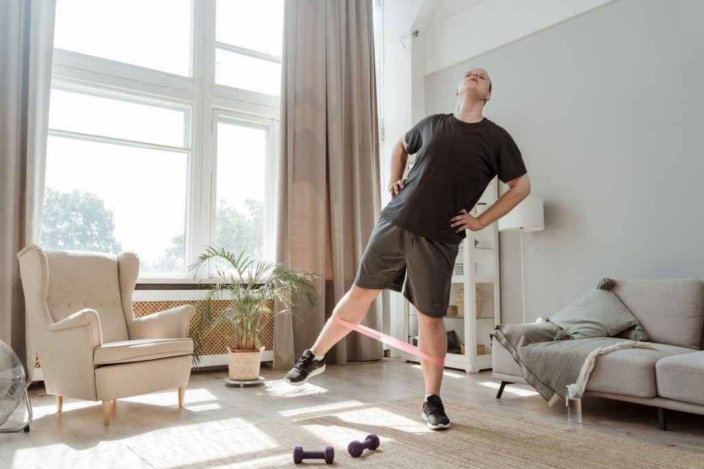 Man performs exercise in living room with resistance band, promoting home fitness.
