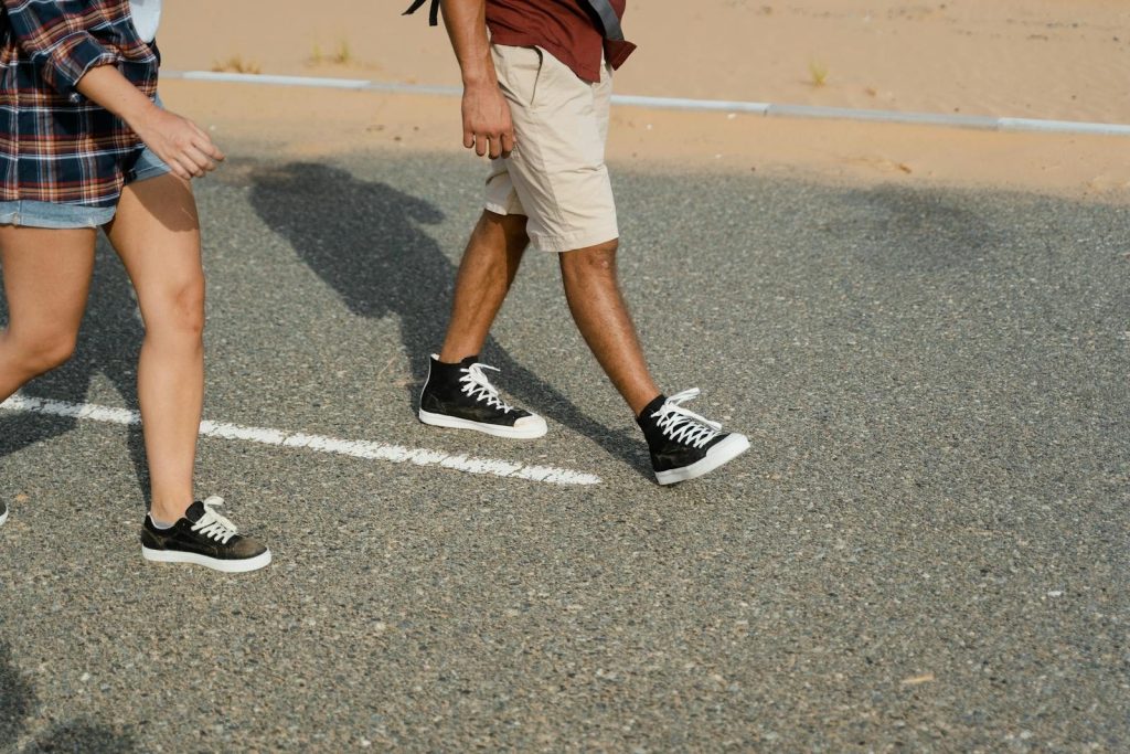 Close-up of two people in sneakers walking down a desert road.