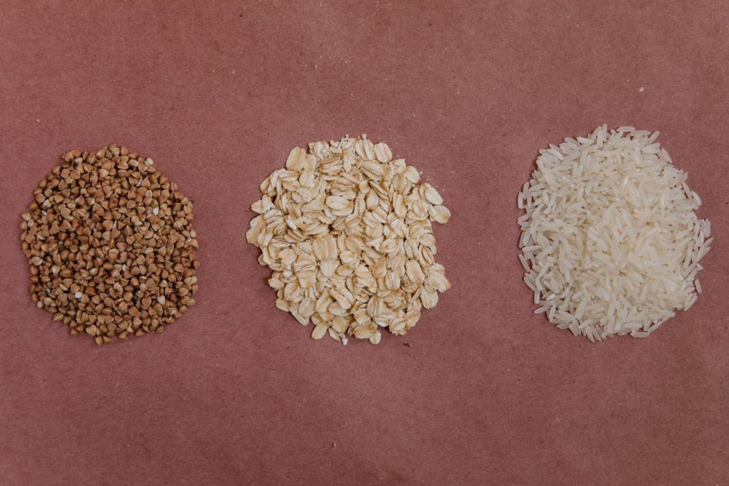 A variety of healthy grains including buckwheat, oats, and rice arranged on a flat surface.