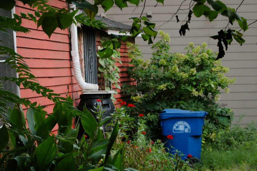 a blue trash can sitting next to a red house