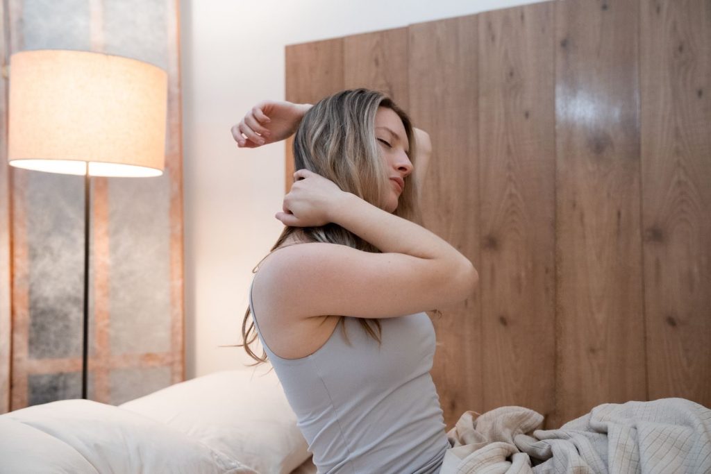 A woman stretching on her bed in a well-lit modern bedroom, evoking a sense of comfort and relaxation.