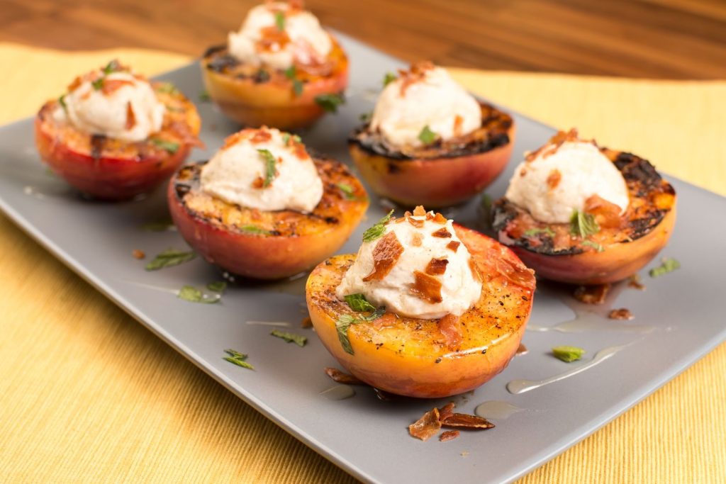 Close-up of grilled peaches topped with cream and herbs on a ceramic plate.