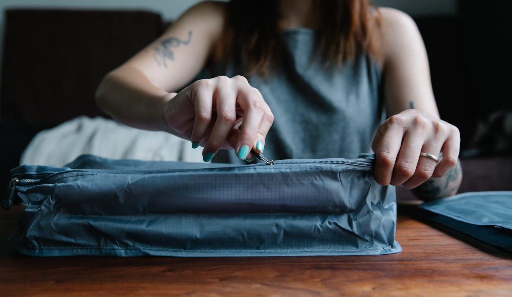 Close-up of a woman with manicured nails zipping a travel bag indoors.