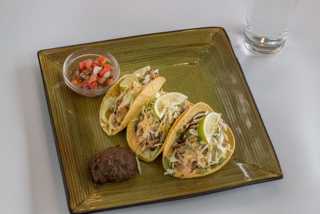 Close-up of freshly prepared tacos with salsa and black bean on a square plate, perfect for food enthusiasts.