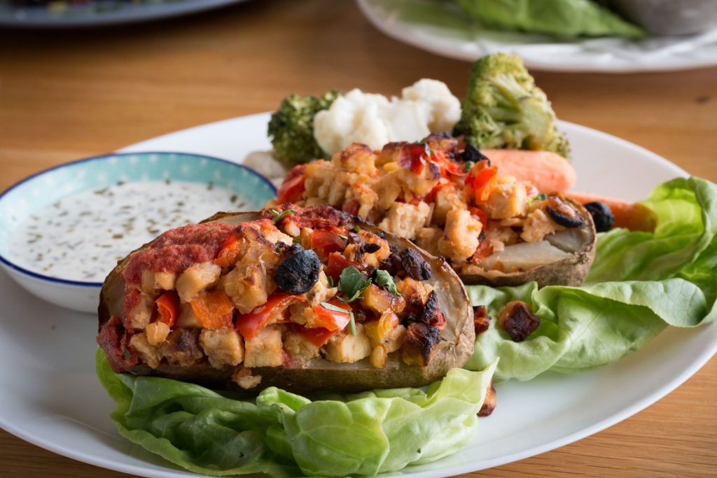 Tasty stuffed baked potato with assorted vegetables and sauce on a white plate.