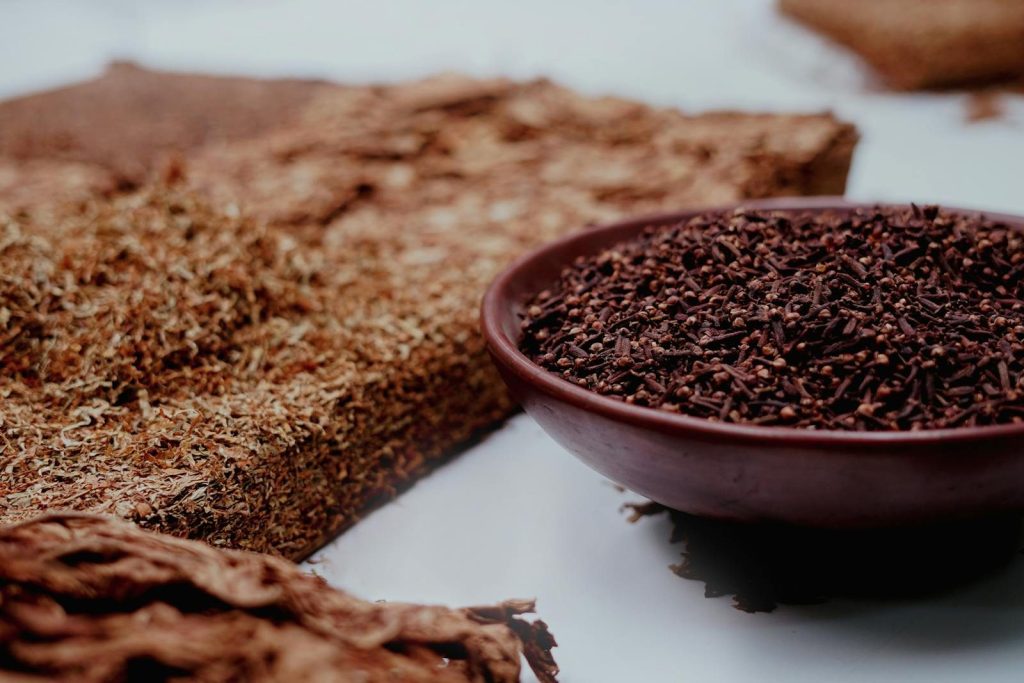Detailed view of aromatic cloves and dried tobacco on a rustic surface.