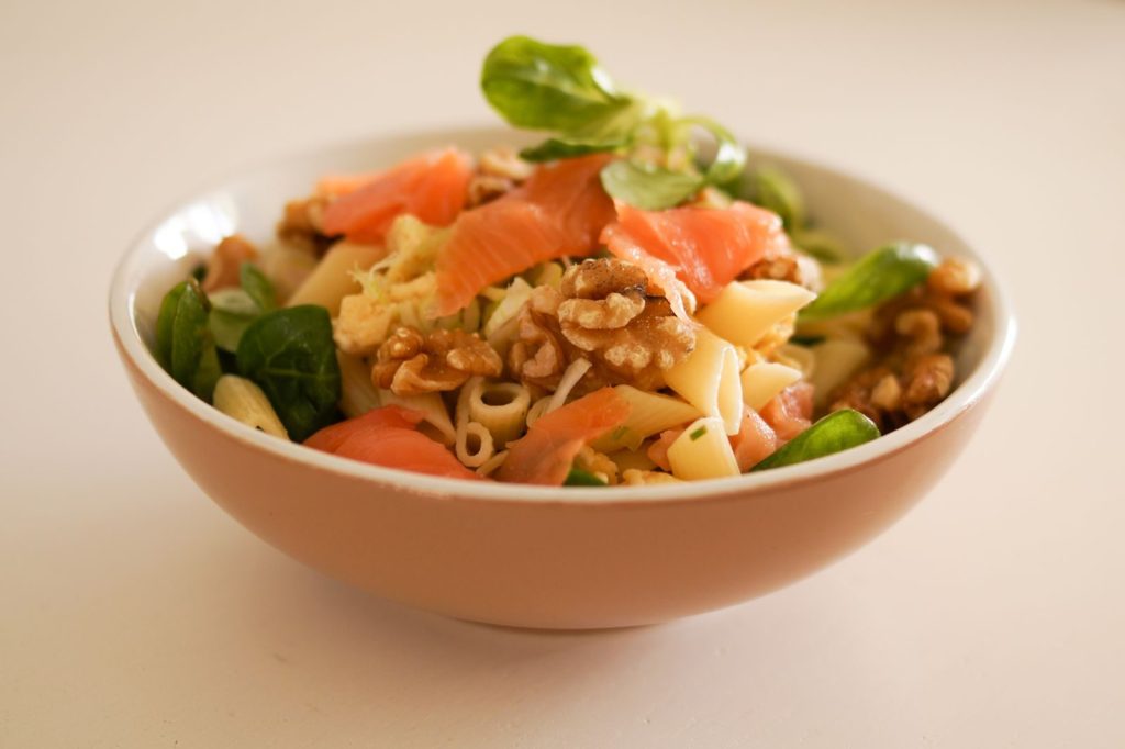 Delicious pasta salad featuring smoked salmon, walnuts, and fresh greens in a ceramic bowl.